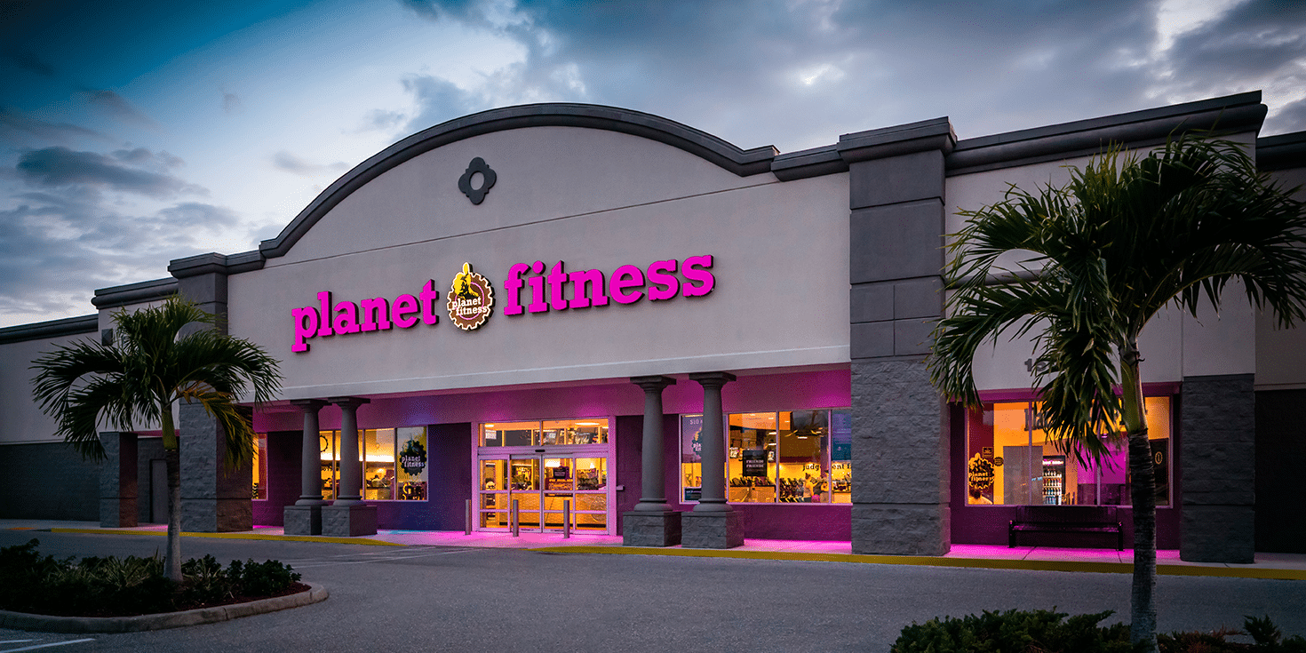 A photo of the planet fitness enterprise in Florida. The interior is glowing yellow and there are palm trees outside.